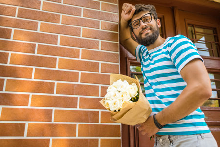 Handsome young man with bouquet of flowers is waiting for his girlfriend. Looking at the camera.の写真素材