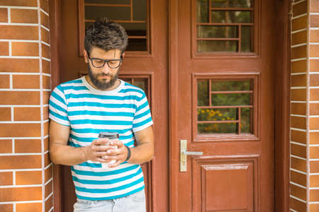 Handsome young man with a cup of coffee is standing near the door.の写真素材