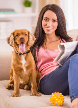 Picture of young woman with a newspaper while her dog is sitting on sofa near her.の写真素材