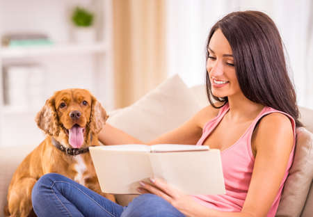 Picture of young woman is reading a book while her dog is sitting on sofa near her.の写真素材