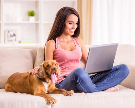 Young woman is working with laptop and her dog sitting on sofa near.