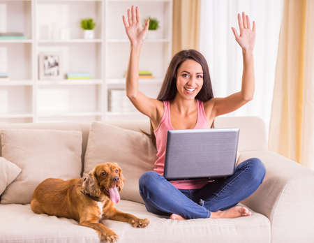 Young woman is working with laptop and her dog sitting on sofa near.の写真素材
