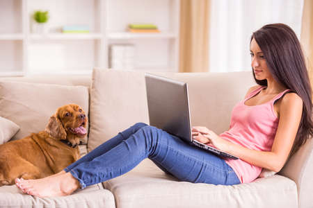 Young woman is working with laptop and her dog sitting on sofa near.の写真素材