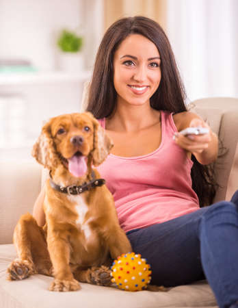 Picture of young woman is watching tv while her dog is lying on sofa near her.の写真素材