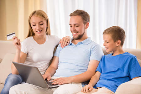 Young happy parent and their teenage son are using laptop sitting on sofa at home.の写真素材