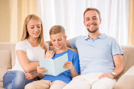 Happy family are reading a book together sitting on sofa at home.の写真素材