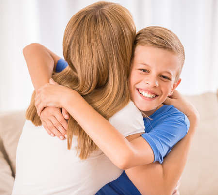 Beautiful woman and her teenage son are hugging at home.の写真素材