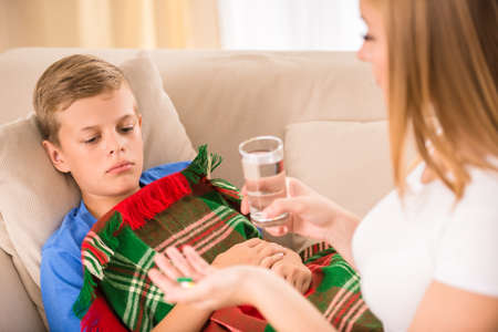 Mother giving a glass of water and pills to her ill son.の写真素材