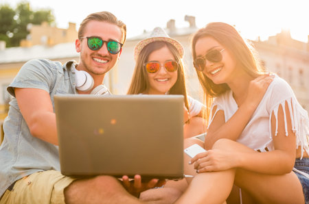 Friendship, leisure and people concept. Young people having a good time together, using laptop, sitting outdoors, in the town.の写真素材