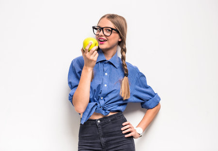Teenage girl is eating an apple, standing on white background.の写真素材