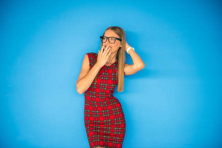 Young beautiful woman in red dress and glasses on blue background.の写真素材