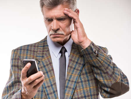 Portrait of senior man is suffering from headache, while looking at telephone.の写真素材