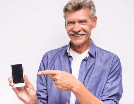 Senior man is using smartphone, standing on white background.の写真素材