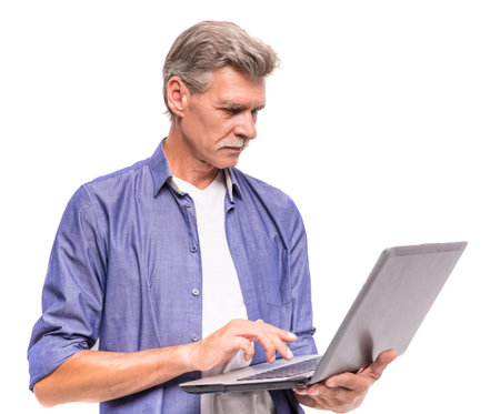 Senior man is using laptop, standing on white background.