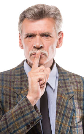 Senior man in suit gesturing silence, standing on white background.の写真素材