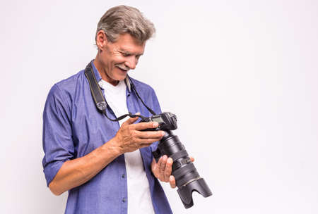 Senior mature man is holding camera while standing against grey background.の写真素材