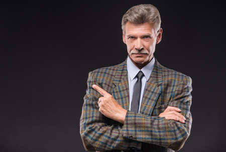 Senior man in suit pointing with finger away.の写真素材