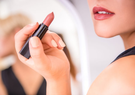 Beautiful young woman is doing makeup, draws lips lipstick.の写真素材