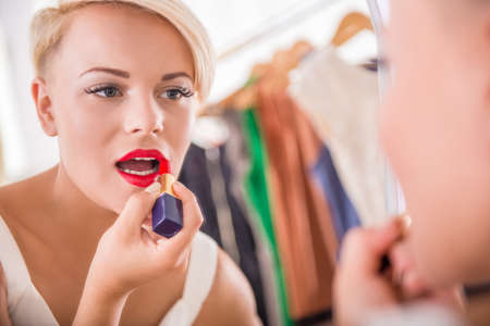 Beautiful young woman is doing makeup, draws lips lipstick.の写真素材