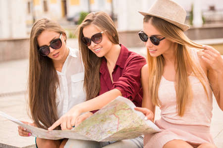 Three beautiful young women walk in the city, using a map, outdoorsの写真素材