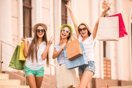 shopping, sale, happy people and tourism concept - three beautiful girls in sunglasses with shopping bags in cityの写真素材
