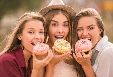 Three beautiful young women, eating cake, outdoorsの写真素材