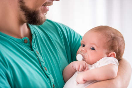 Portrait of young happy father with a baby at homeの写真素材