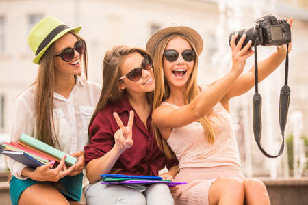 Three beautiful young women walk in the city, use the camera, outdoorsの写真素材