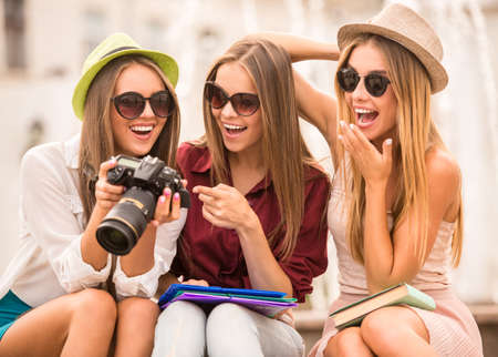 Three beautiful young women walk in the city, use the camera, outdoorsの写真素材