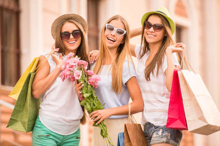 shopping, sale, happy people and tourism concept - three beautiful girls in sunglasses with shopping bags in cityの写真素材