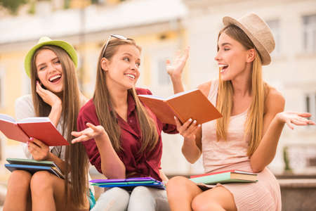 Three beautiful young female students sitting on a park bench in summerの写真素材