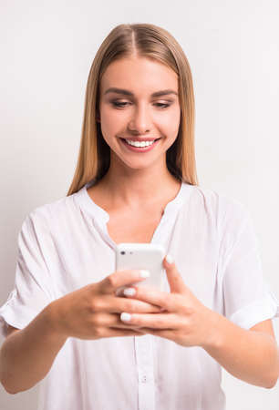 Portrait of a young, beautiful woman, using the phone on a gray background. Studio shootの写真素材