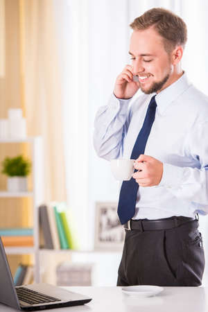 Young businessman drinking coffee and using a laptop in the officeの写真素材