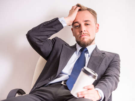 Portrait of tired young businessman drinking coffee on white backgroundの写真素材