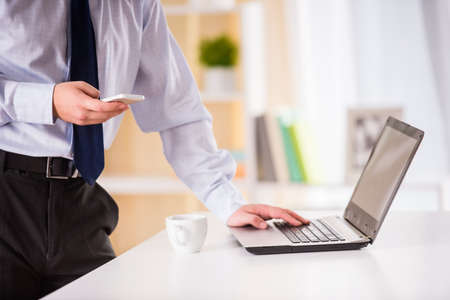 Young businessman drinking coffee and using a laptop in the officeの写真素材