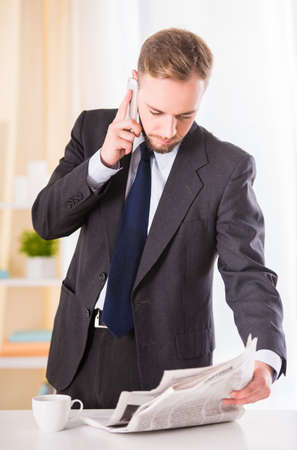 Young businessman drinking coffee and reading the newspaperの写真素材