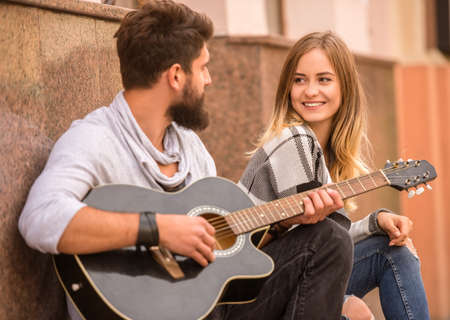 Portrait of a young happy couple playing guitar while standing on a ladder in cityの写真素材