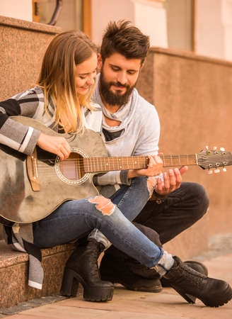 Portrait of a young happy couple playing guitar while standing on a ladder in cityの写真素材