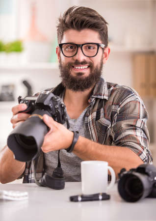 Young cheerful photographer with beard, while working in his officeの写真素材