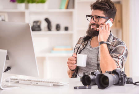 Young cheerful photographer with beard, while working in his officeの写真素材