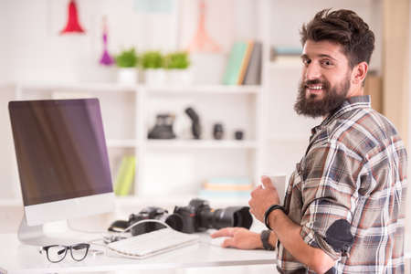 Young cheerful photographer with beard, while working in his officeの写真素材