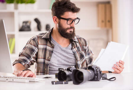 Young cheerful photographer with beard, while working in his officeの写真素材