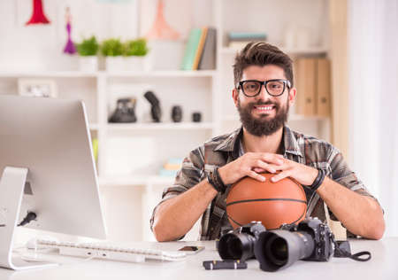 Young cheerful photographer with beard, while working in his officeの写真素材