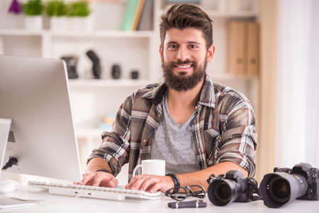Young cheerful photographer with beard, while working in his officeの写真素材