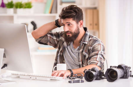 Young cheerful photographer with beard, while working in his officeの写真素材