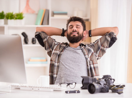 Young cheerful photographer with beard, while working in his officeの写真素材