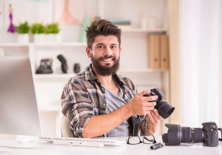 Young cheerful photographer with beard, while working in his officeの写真素材