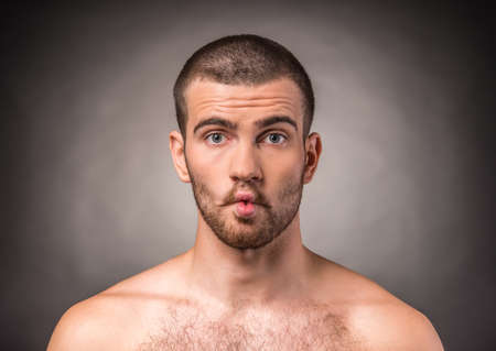 Portrait of an emotional young man with a naked torso on a black backgroundの写真素材