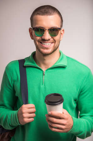 Portrait of a young man drinking coffee on a gray background. Studio shootingの写真素材