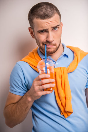 Portrait of cheerful young man drinking juice on a gray backgroundの写真素材